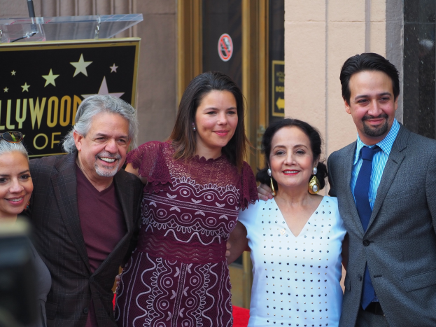Gruppe von Menschen auf einem roten Teppich bei der Zeremonie der Hollywood Walk of Fame mit einer Kamera im Hintergrund, einer Tafel mit Text, einem Glaspodest und einer Wand.