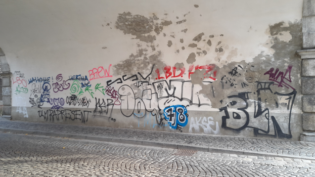 Eine Wand mit bunten und verschiedenen Graffiti neben einem Gebäude, mit einer Straße unten.