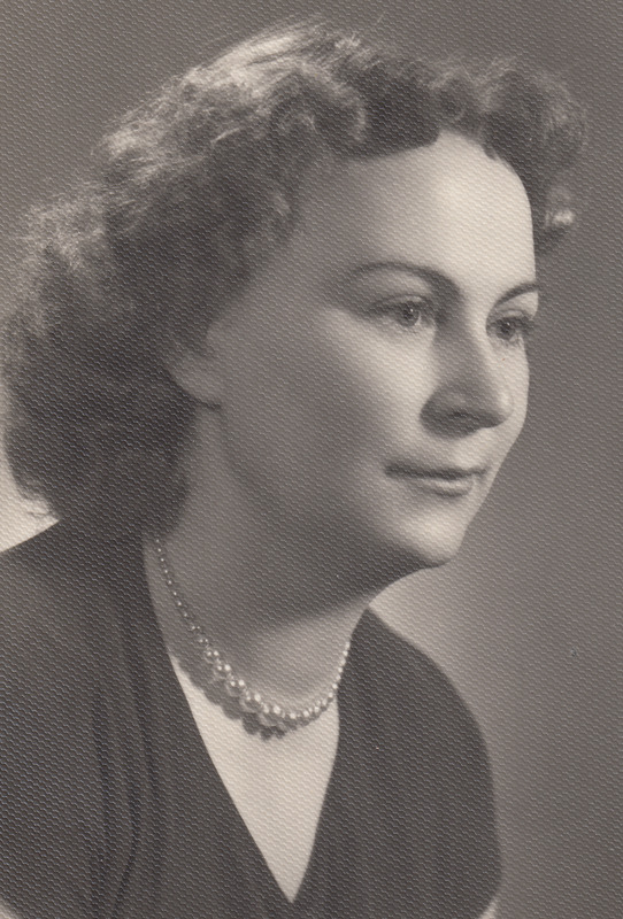 Ein Schwarz-Weiß-Foto einer Frau mit ernstem Gesichtsausdruck, die eine Kette trägt und ein einfaches Kleid mit hohem Kragen und langen Ärmeln trägt, ihr Haar ist zurückgebunden und ihre Augen sind fokussiert.