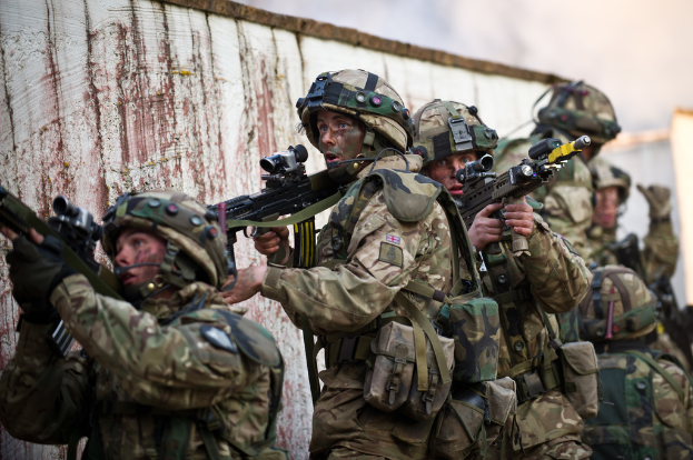 Soldaten neben einer Wand mit jeweils einem Gewehr in der Hand.