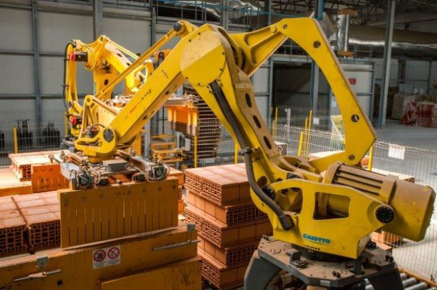 Großes industrielles Lager mit gestapelten Kisten, Überheadkranen, Zaun, Pfählen und einer fernen Wand in einer automatisierten Fertigungsumgebung.