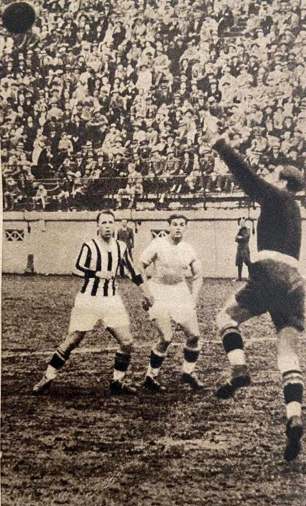 Schwarzes und weißes Foto von Männern, die auf einem Feld Fußball spielen, mit Zuschauern auf den Tribünen und einer Wand im Hintergrund, beschriftet mit "Newcastle United v West Bromwich Albion".