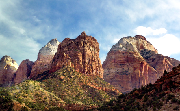 Eine malerische Aussicht auf den Zion-Nationalpark in Utah mit majestätischen Bergen, dichtem Wald, felsigem Gelände und einem Himmel mit weißen Wolken.