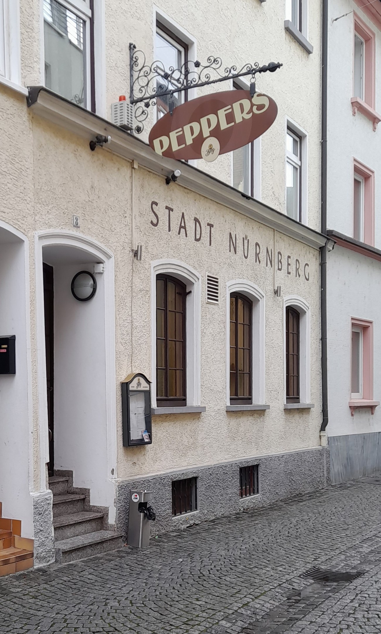 Gebäude mit einer "Stadt Nurnberg"-Aufschrift, Fenstern, einer Tür, einer Treppe und einem Müllcontainer im Vordergrund.