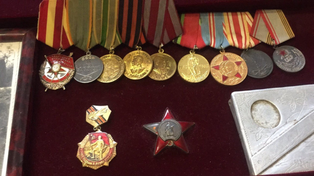 Eine hölzerne Box mit verschiedenen Medaillen, darunter ein roter Stern, ordentlich mit einem Objekt auf der rechten Seite.