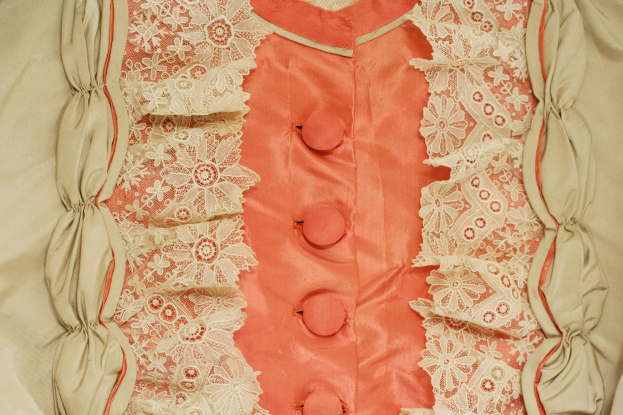 Nahaufnahme eines rosafarbenen und cremefarbenen Kleides mit weißer Spitze und Frontknöpfen, das eine klassische und elegante Design zeigt.