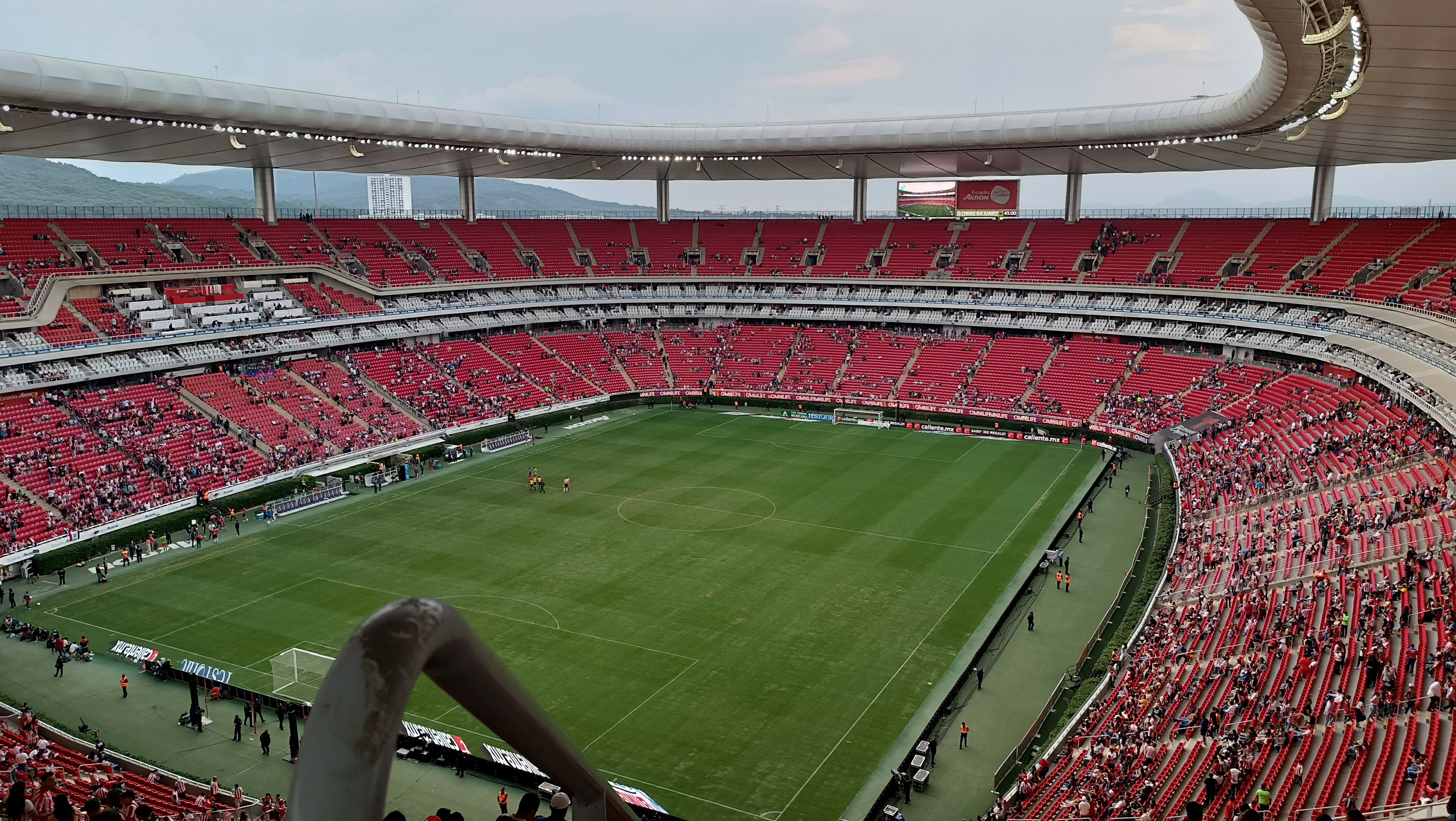 Ein großes Stadion voller Zuschauer, die ein Fußballspiel sehen, mit Hügeln und einem klaren blauen Himmel im Hintergrund.
