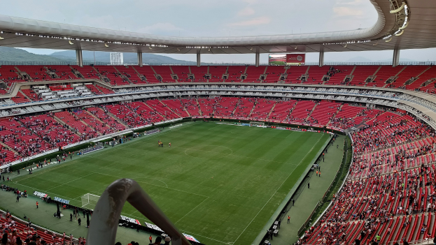 Ein großes Stadion voller Zuschauer, die ein Fußballspiel sehen, mit Hügeln und einem klaren blauen Himmel im Hintergrund.