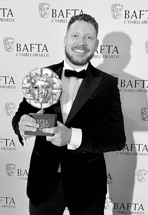 Ein Mann im Smoking, der eine BAFTA-Trophäe hält und vor einer Tafel mit der Aufschrift "BAFTA Awards 2018" steht
