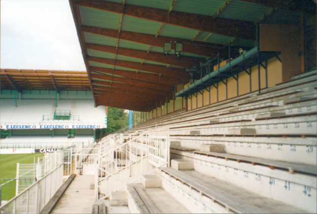 Ein altes Foto eines Stadions mit zahlreichen Sitzplätzen, Geländern, Treppen, einem Schuppen, Tafeln mit gedrucktem Text, Gras, Bäumen und einem Himmel im Hintergrund.