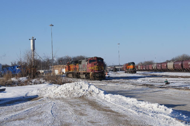 Eine Lokomotive vorne mit einem Waggon auf der rechten Seite, auf Gleisen geparkt mit Schnee auf dem Boden, trockenen Bäumen und einem Strommast im Hintergrund.