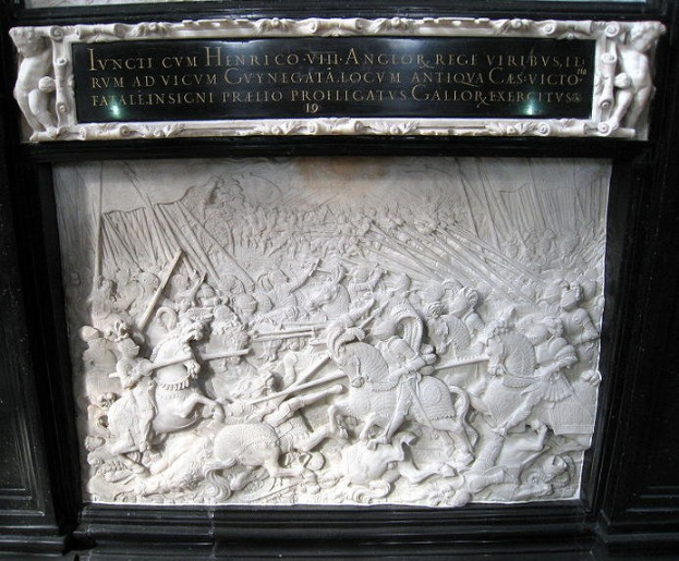 Weißer Marmorplatten mit schwarzem Rand an einem Gebäude, die eine Schlacht mit Schwertern und Schilden haltenden Figuren darstellen, umgeben von Zuschauern.