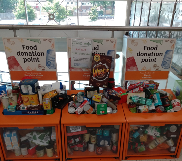 Orange Schränke mit Lebensmitteln wie Flaschen, Dosen und Kartons, neben Texttafeln, mit Blick auf Fahrzeuge, Bäume, Gebäude und Himmel durch Glasfenster.