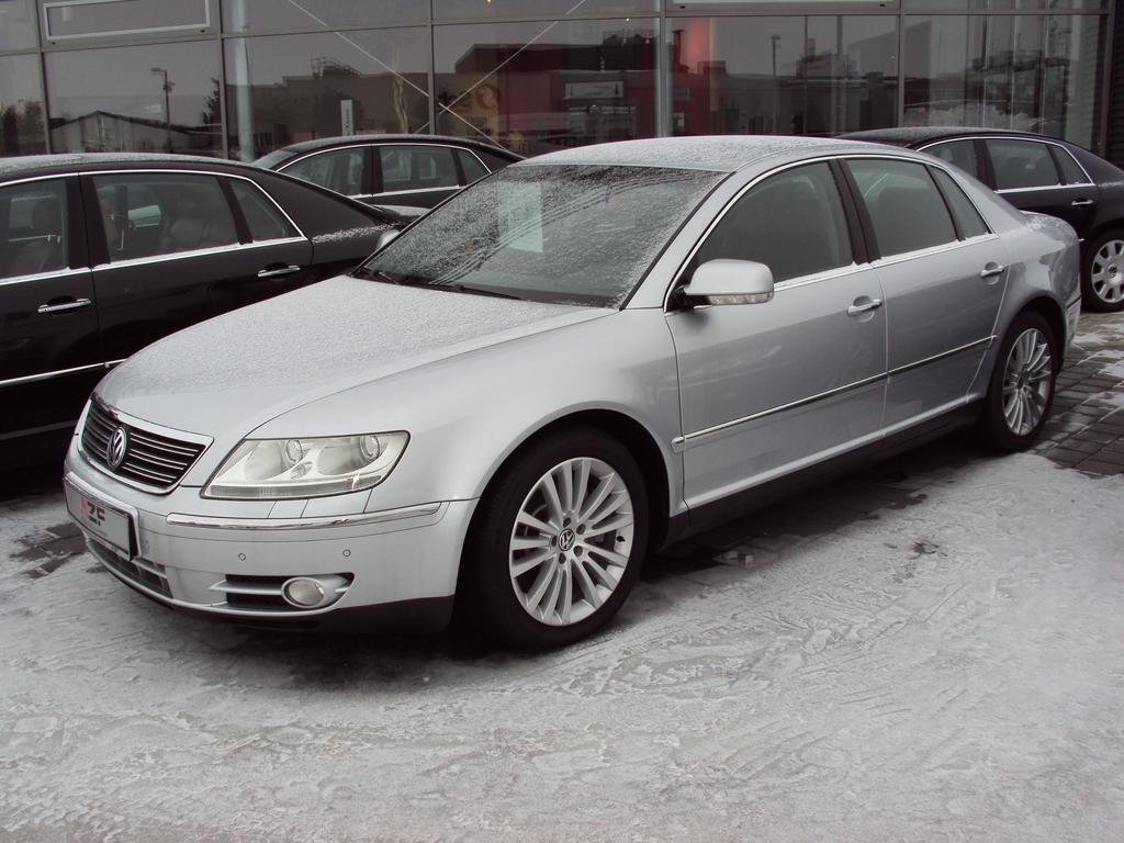 Ein Auto steht auf einem verschneiten Gehweg vor einem Glasgebäude mit drei weiteren Autos im Hintergrund.