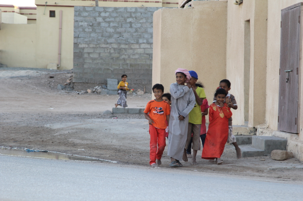 Eine Gruppe strahlender Kinder, die vor Gebäuden, Wasser, Felsen und einer Straße stehen