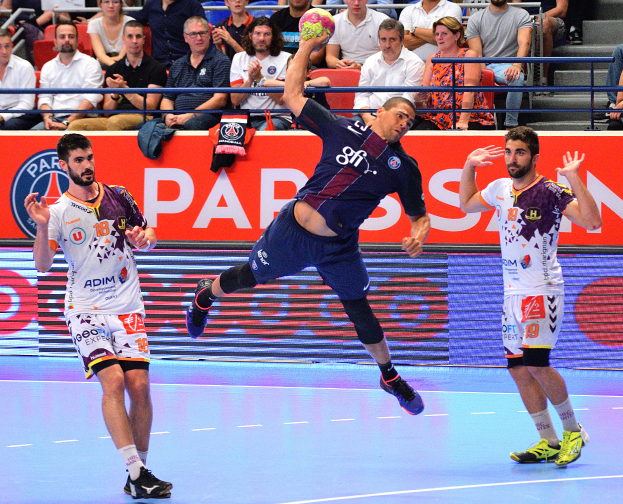 Männer spielen Handball auf einem Feld mit einem Ball in der Mitte, Zuschauer im Hintergrund und einem Banner mit der Aufschrift "Futsal-Weltmeisterschaft 2015 - Paris Saint-Germain vs. Olympique Lyon."