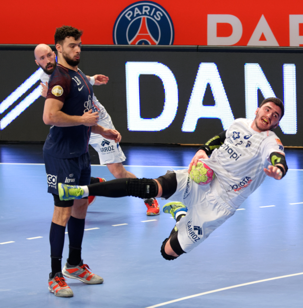 Eine Gruppe von Männern, die auf einem Platz Handball spielen, einer hält den Ball, mit einem Paris Saint-Germain-Futsal-Team-Schild im Hintergrund.