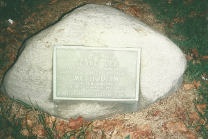 Ein großer Felsen mit einer Tafel, auf der "Jesse Lee Methodism" steht, umgeben von trockenem Laub und Gras.