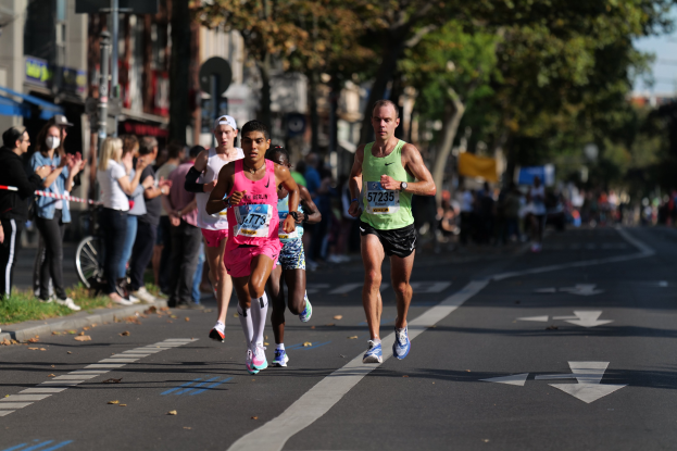 Gruppe von Menschen, die bei einem Marathon auf einer Stadtstraße laufen, mit Zuschauern und unscharfem städtischem Hintergrund.