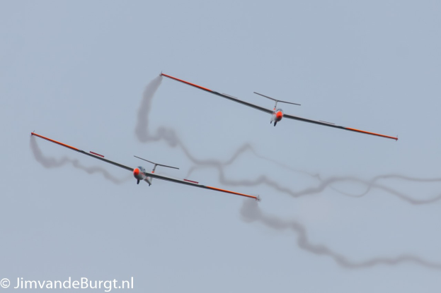 Zwei Segelflugzeuge am Himmel mit Rauchspuren, Text in der linken unteren Ecke.