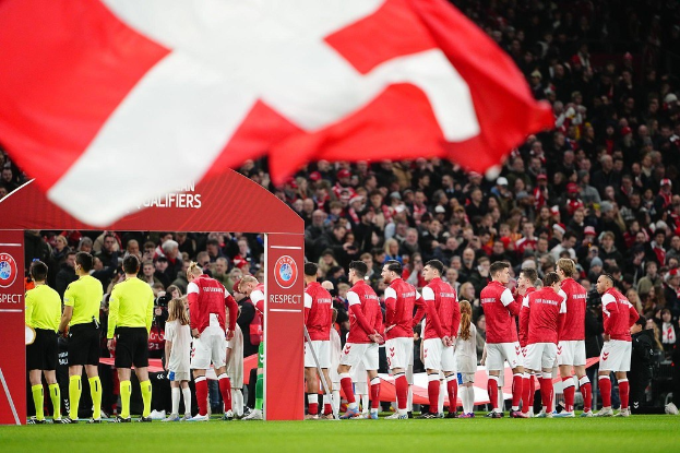 Gruppe von Menschen auf einem Fußballfeld mit einer roten und weißen Flagge im Vordergrund, einem Bogen mit der Aufschrift "Bayern München vs. Bayern München Wetten Tipps & Vorschau" im Hintergrund und einer großen Menge im Stadion.