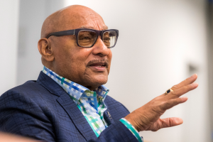 Ein Mann in Anzug und Brille spricht in ein Mikrofon und spricht vor einem unscharfen Hintergrund zu einem Publikum.