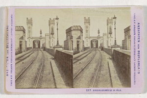 Schwarz-weißes stereoskopisches Bild einer Eisenbahnbrücke in Köln, Deutschland, das Eisenbahninfrastruktur, Umgebungswände, Pfosten, Statuen, Himmel und Text zeigt.