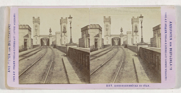 Schwarz-weißes stereoskopisches Bild einer Eisenbahnbrücke in Köln, Deutschland, das Eisenbahninfrastruktur, Umgebungswände, Pfosten, Statuen, Himmel und Text zeigt.
