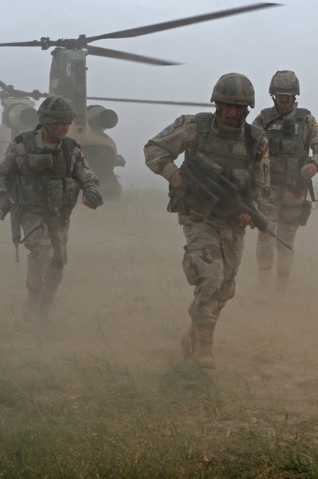 Drei Personen mit Waffen rennen, im Hintergrund ein Hubschrauber und Gras und Boden darunter.