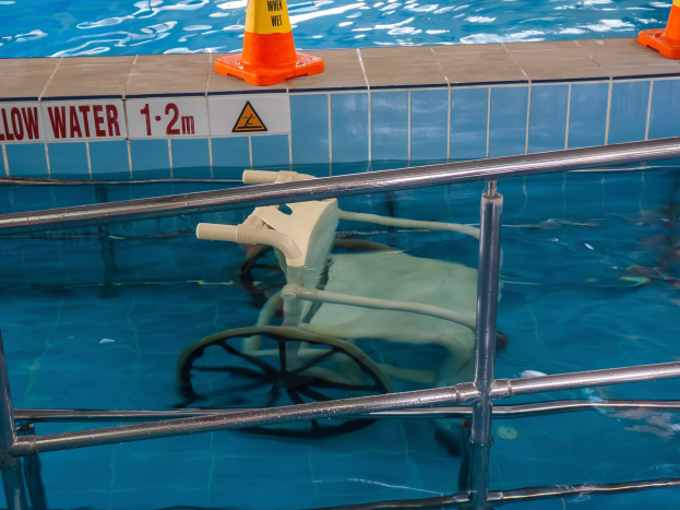 Ein Schwimmbad mit einem Stuhl in der Mitte, umgeben von Sicherheitskegeln und einem Geländer, und ein Schild an der Wand, das verfügbare Schwimmausrüstung anzeigt.