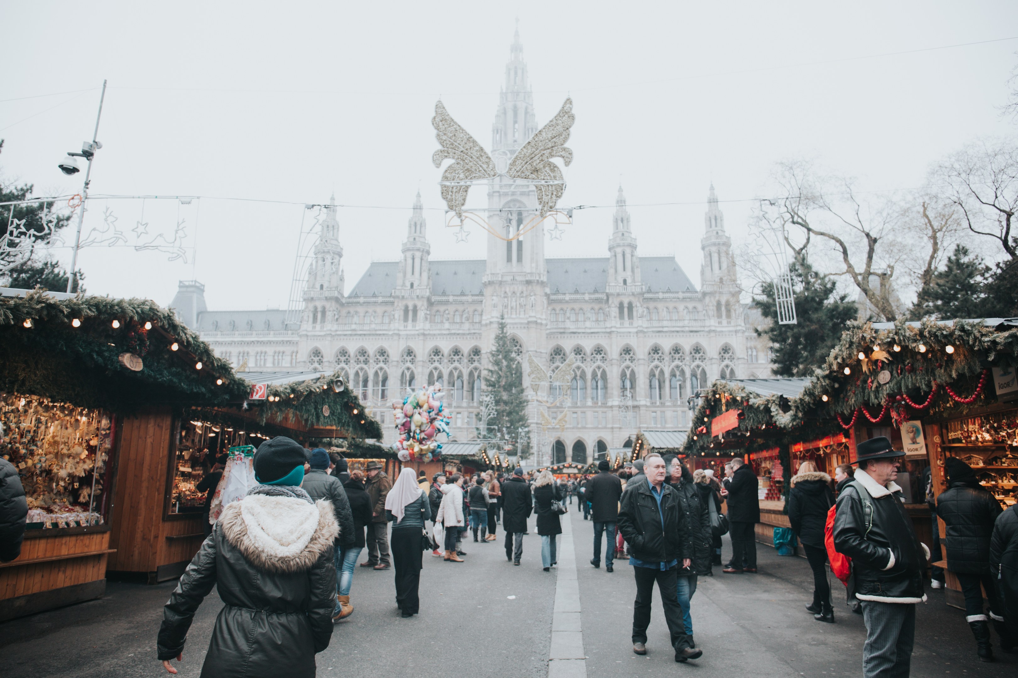 Ein lebendiger Weihnachtsmarkt in Wien, Österreich, mit Menschen, die herumlaufen, Ständen, die mit Lichtern und festlichen Décorations geschmückt sind, einem Gebäude mit Fenstern im Hintergrund, Bäumen und einem klaren blauen Himmel.