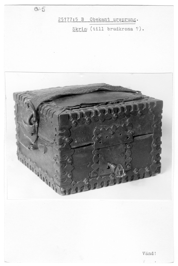 Schwarzes und weißes Foto einer kleinen hölzernen Kiste mit einem Schloss auf einer weißen Oberfläche, die an eine Schatzkiste erinnert.