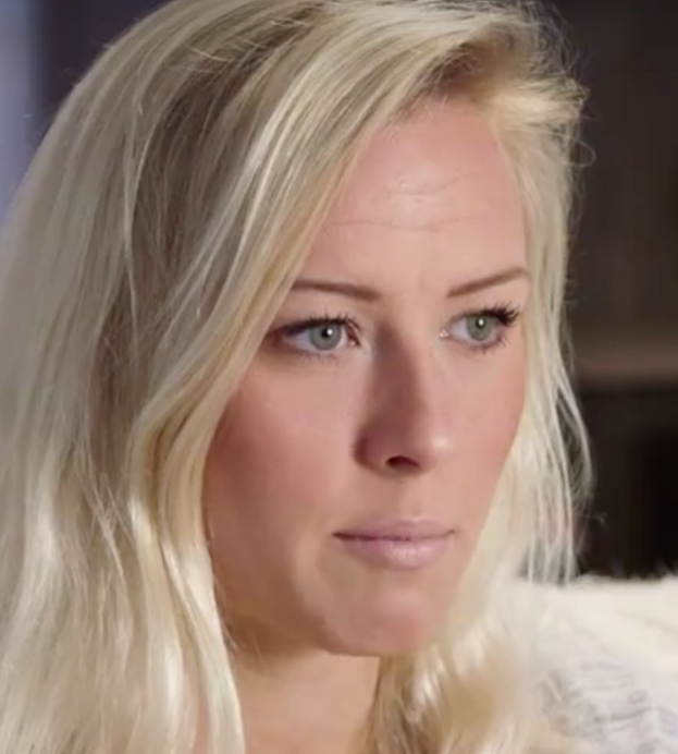 Blonde Frau mit blauen Augen im Vordergrund, Hintergrund unscharf, sieht besorgt aus.