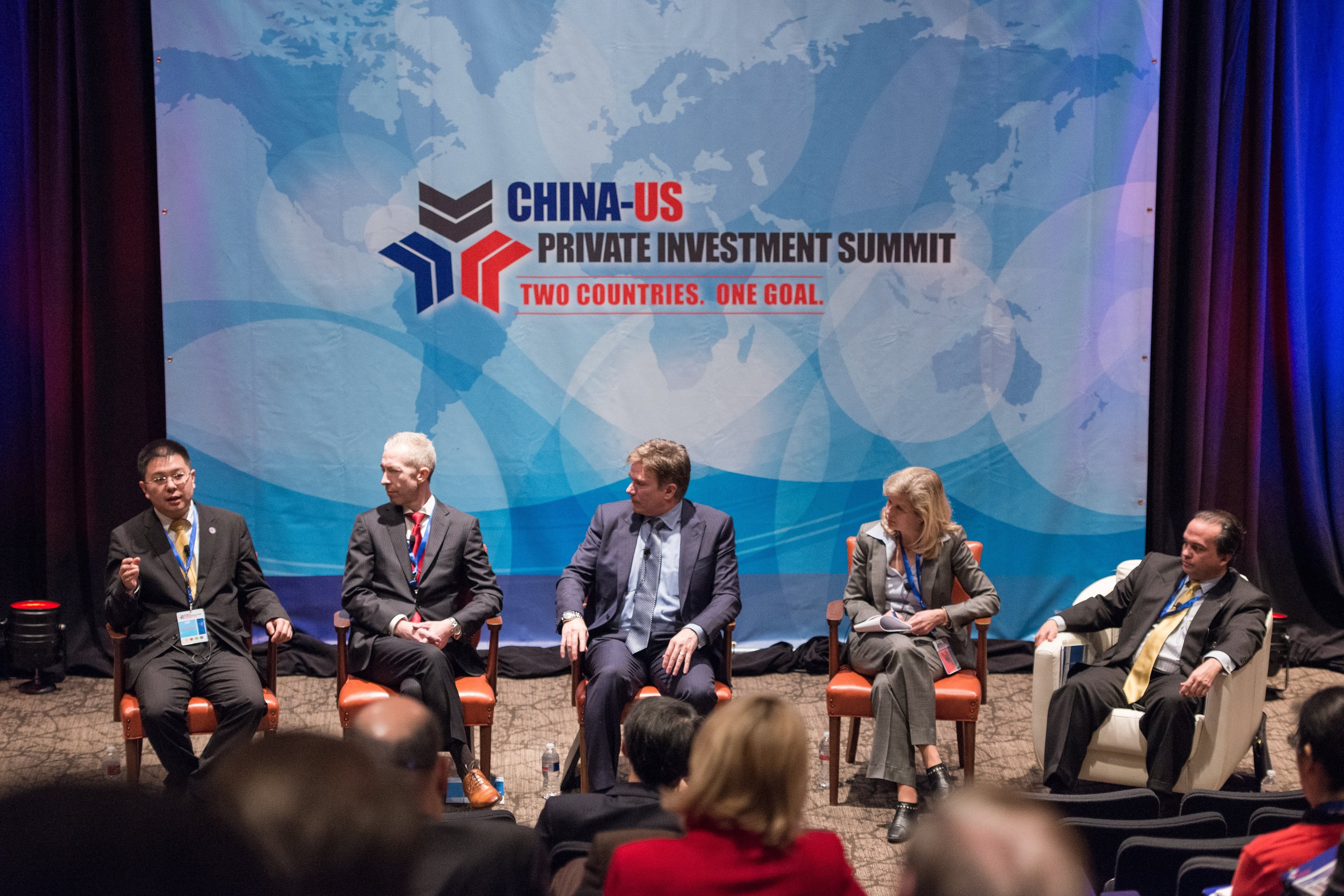 Gruppe von Menschen, die auf Stühlen sitzen und einem Bildschirm mit Text und einer Karte sowie Vorhängen im Hintergrund zugewandt sind, was auf einen China-US-Privatinvestment-Gipfel hindeutet.