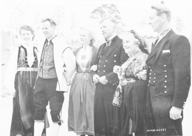 Eine Gruppe von Menschen in den 1930er Jahren, die gemeinsam draußen stehen, lächeln und von Bäumen im Hintergrund umgeben sind, mit der Aufschrift 'Bayerische Familie in den 1930er Jahren' unten.