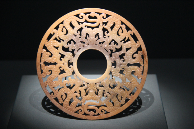 Ein chinesischer geschnitzter Jade-Teller in einem Museum ausgestellt, mit detaillierten Oberflächenverzierungen und einem dunklen Hintergrund.