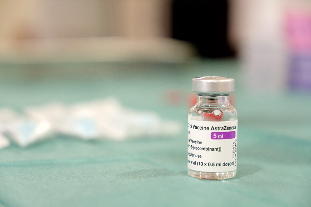 Ein Fläschchen AstraZeneca-Impfstoff auf einem grünen Tisch umgeben von verstreuten weißen Papieren, mit einem unscharfen Hintergrund.