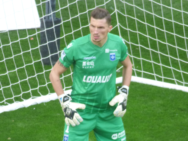 Ein Torwart in grüner Uniform steht vor einem Fußballtor auf saftig grünem Rasen, Handschuhe tragend.