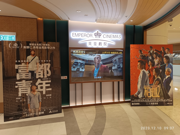 Eintritt zum Emperor Cinemas in Hong Kong mit Bannern, einem Bildschirm, einer Namensschild, Deckenbeleuchtung und einem Wasserzeichen.