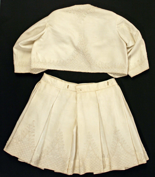 Weißer knielanger Faltenrock mit hohem Bund und ärmelloser Rundhalsbluse auf schwarzem Hintergrund, beide aus leichtem Stoff mit feiner Schimmer.