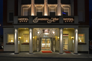 Das Essenerhof Hotel in Berlin, Deutschland, ein mehrstöckiges Gebäude mit Fenstern, Türen und Säulen, hat ein Namensschild und liegt entlang einer Straße mit Fahrzeugen auf der rechten Seite, unter einem sichtbaren Himmel.