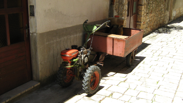 Ein Traktor mit einem Anhänger auf einer StraÃŸe, mit einem Haus mit Türen daneben.