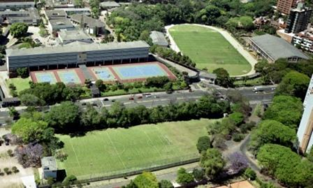 Luftaufnahme eines Fußballfelds an der Universität Sydney, umgeben von Bäumen, Gebäuden und Fahrzeugen, mit einem neuen Sportkomplex in Entwicklung.