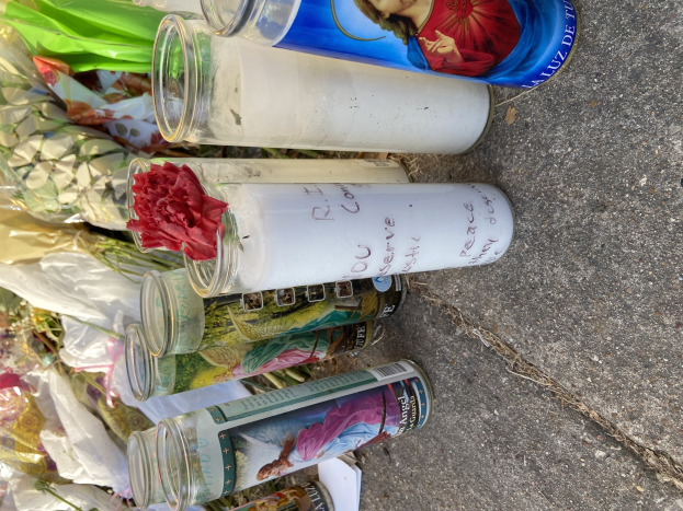Provisorisches Straßenrand-Denkmal mit Glasflaschen mit Fotos und Text, einem Blumenstrauß und brennenden Kerzen.