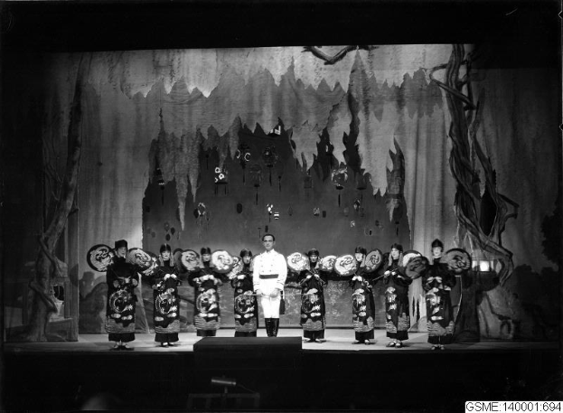 Schwarzes und weißes Foto von Darstellern in traditionellen japanischen Kimonos auf einer Bühne mit einer gemalten Kulisse, beschriftet mit "Kimono-Show in Tokyo, Japan."