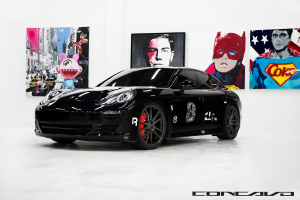 Ein schwarzer Nissan-Sportwagen mit Cartoon-Postern im Hintergrund und einem kleinen Zitat unten.