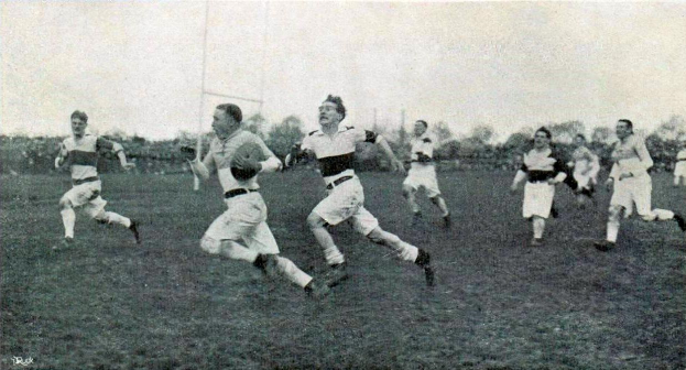 Eine Gruppe von Männern, die Rugby auf einem grasbewachsenen Feld mit Bäumen und Pfosten im Hintergrund spielen, unter einem klaren Himmel, mit dem Text "1930s rugby league" unten, in Schwarz-Weiß.