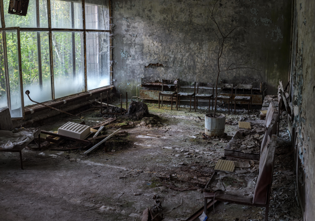Ein verlassener Krankenhausraum in Pripyat, Tschernobyl, Ukraine, mit Stühlen, Tischen und anderen Gegenständen, abblätternder Farbe an den Wänden und durch die Glasfenster sichtbaren Bäumen.