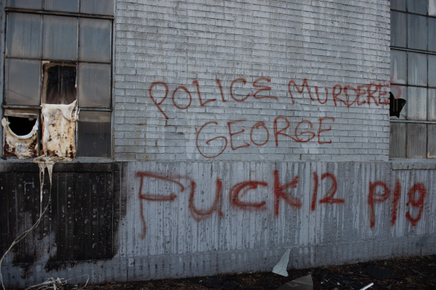 Graffiti auf einer Gebäudewand mit der Aufschrift "Polizei Mord George Fuck 12 P19" und Fenstern sowie verstreuten Gegenständen davor.