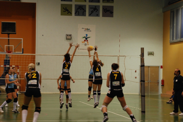 Ein Volleyballspiel im Indoor-Court mit einem Basketballkorb im Hintergrund.